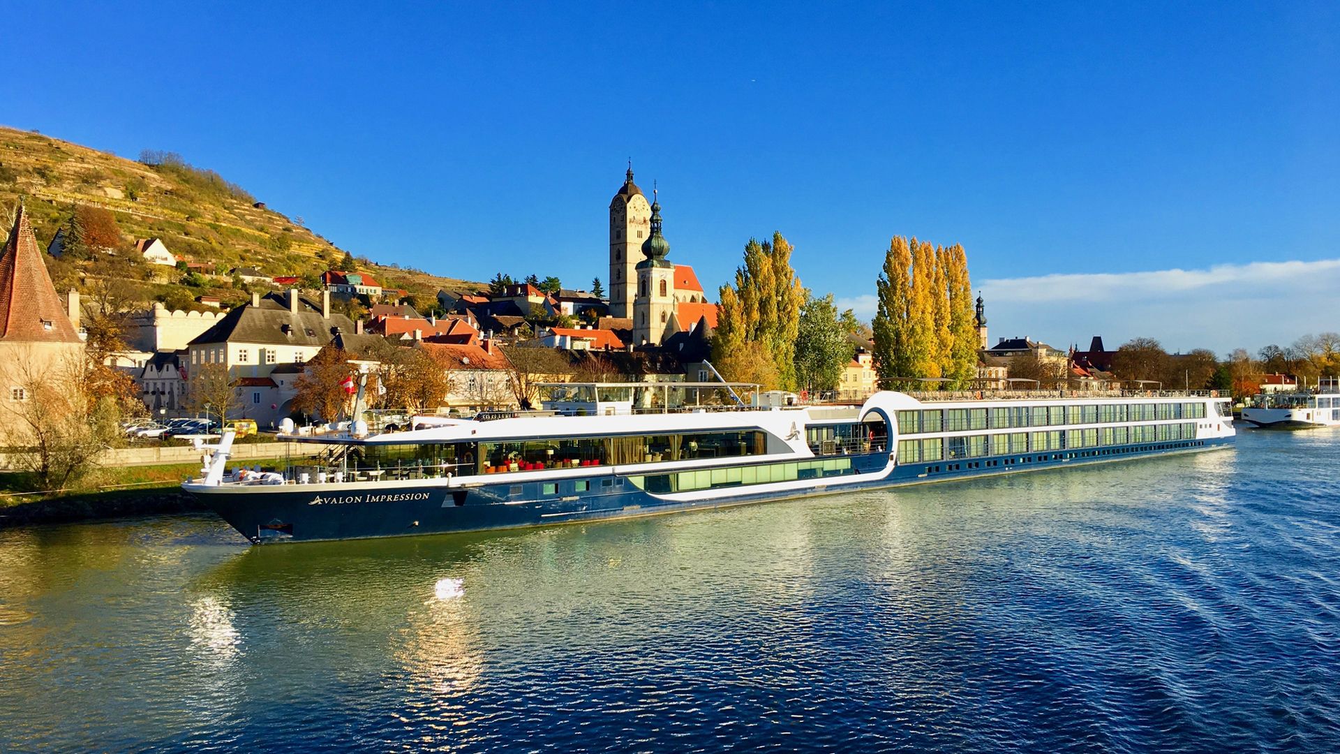 River cruise ship passing a hillside village with a church tower in autumn